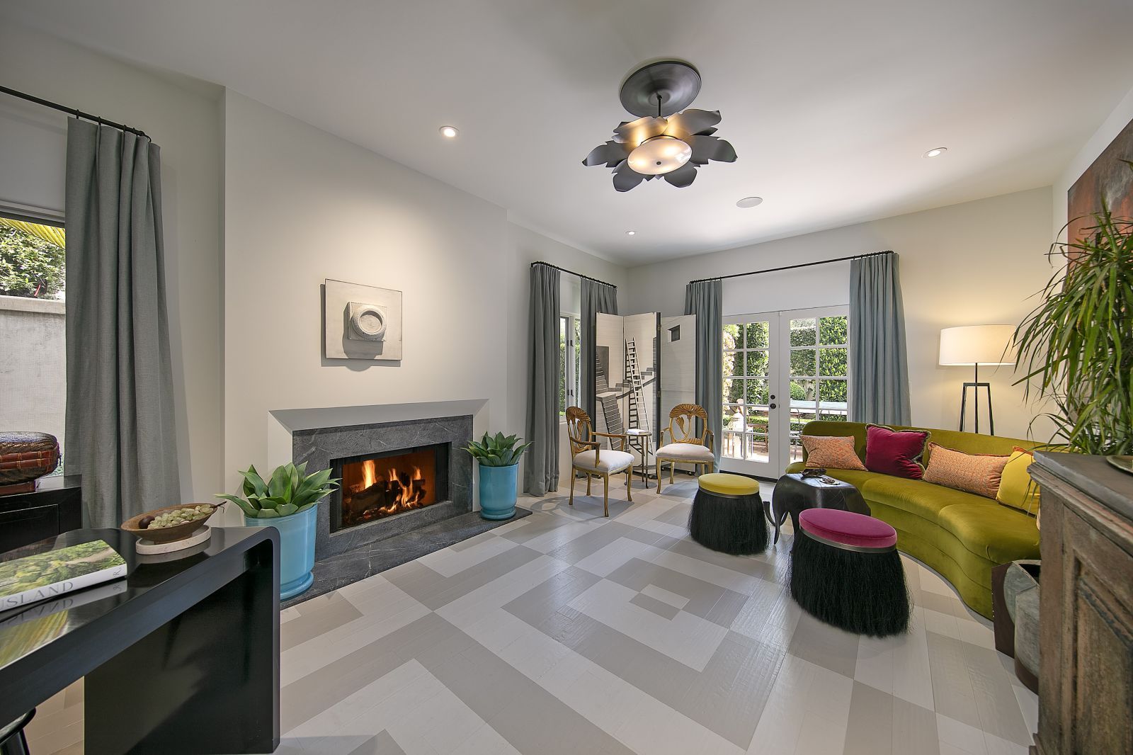 An intimate sitting room of a luxury home, with fire in the fireplace and glass doors to a terrace.